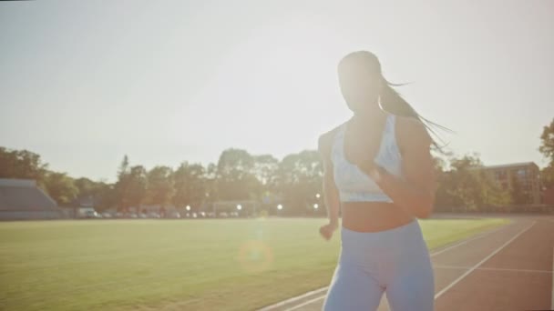 Красива фітнес-жінка в легкому блакитному атлетичному верху і легінси біг на стадіоні. Вона біжить в тепле літо вдень. Спортсменка робить свою спортивну практику на трасі. Повільний рух . — стокове відео