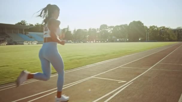 Mooie fitness vrouw in licht blauwe atletische top en legging joggen in een stadion. Ze loopt op een warme Zomermiddag. Atleet doet haar routine sportpraktijk op een spoor. Slow Motion. — Stockvideo