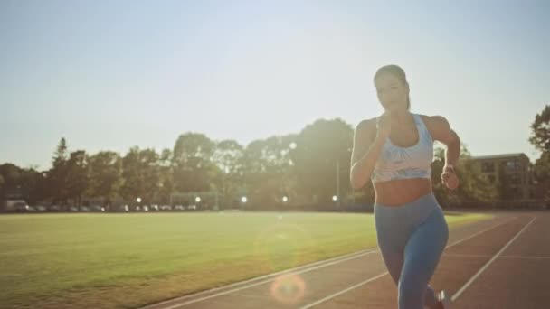 Hermosa mujer de fitness en la parte superior atlética azul claro y leggings corriendo en un estadio. Ella está corriendo en una cálida tarde de verano. Atleta haciendo su práctica deportiva de rutina en una pista. Moción lenta . — Vídeos de Stock