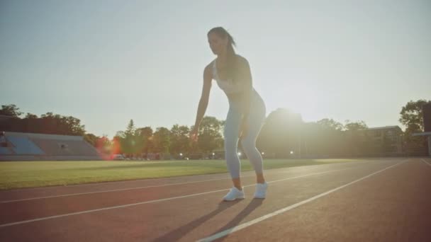 Belle femme de remise en forme en haut et leggings athlétiques bleu clair commence une course de sprint dans un stade extérieur. Elle court un jour d'été chaud. Athlète faisant sa pratique sportive. — Video