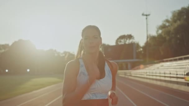 Mooie fitness vrouw in licht blauwe atletische top joggen in een buiten stadion. Ze loopt op een warme Zomermiddag. Atleet doet haar sportpraktijk op een spoor. Portret schot. — Stockvideo