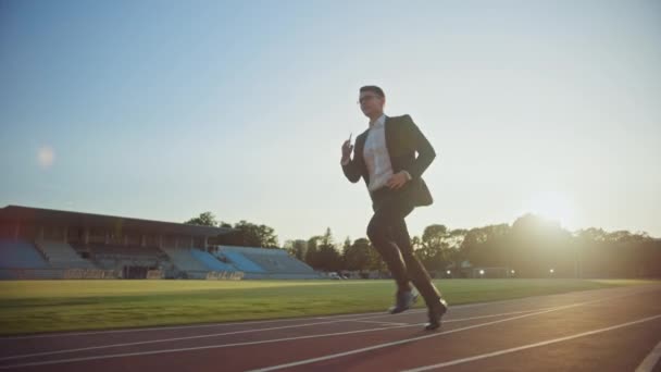 Young Serious Businessman in a Suit Running in an Outdoors Stadium (en inglés). Lleva gafas y sostiene un teléfono móvil. Trabajador de oficina persiguiendo objetivos. Sátira gerencial. Disparo de cámara lenta . — Vídeos de Stock