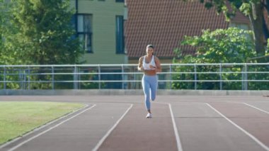 Açık Mavi Atletizm Üstündeki Mutlu ve Gülümseyen Spor Kadını ve Bir Stadyumda Koşu Yapıyor. Sıcak bir yaz öğleden sonrasında koşuyor. Sporcu, Rutin Spor Uygulamasını Pistte Yapıyor.