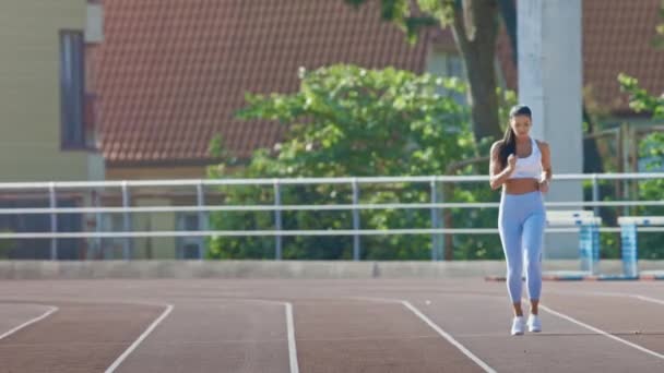 Mooie fitness vrouw in licht blauwe atletische top en legging joggen in een stadion. Ze loopt op een warme Zomermiddag. Atleet doet haar routine sportpraktijk op een spoor. Slow Motion. — Stockvideo