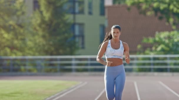 Щаслива і усміхнена фітнес-жінка в легкому блакитному атлетичному верху і легінси біг на стадіоні. Вона біжить в тепле літо вдень. спортсмен робить свою практику на треку . — стокове відео