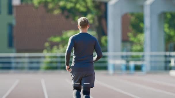 Smiling Athletic Fit Man in Grey Shirt and Shorts Jogging in the Stadium. Está corriendo rápido en una cálida tarde de verano. Atleta haciendo su práctica deportiva rutinaria. Disparo de cámara lenta . — Vídeos de Stock