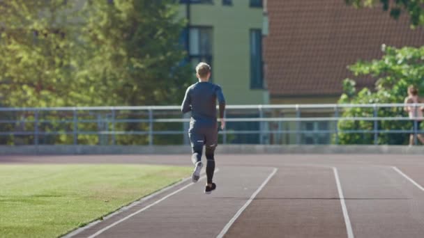 Leende atletisk passar mannen i grå skjorta och shorts jogging på arenan. Han springer fort på en varm sommar eftermiddag. Idrottsman gör sin rutinmässiga idrottsutövning. Slow motion shot. — Stockvideo