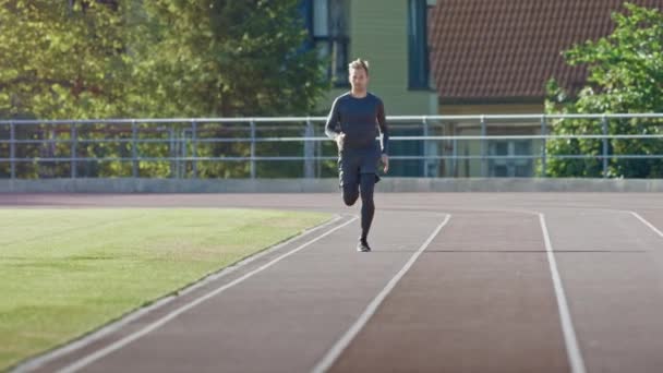 Usmívající se atletický muž v šedé košili a trenýrkách s joggerem na stadionu. V teplém letním odpoledni běží rychle. Sportovec dělá svou rutinní sportovní praxí. Výstřel z pomalého pohybu. — Stock video