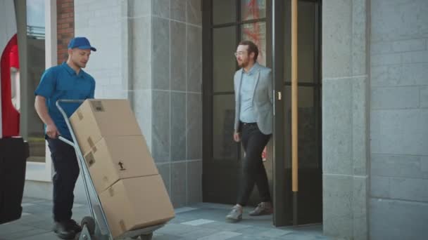 Доставка Чоловік штовхає візок ручної вантажівки, наповнений картонними коробками Пакет рук Клієнту, який потім підписує електронний пристрій Pod. Кур'єр надає посилку людині в стильному сучасному районі міського офісу — стокове відео