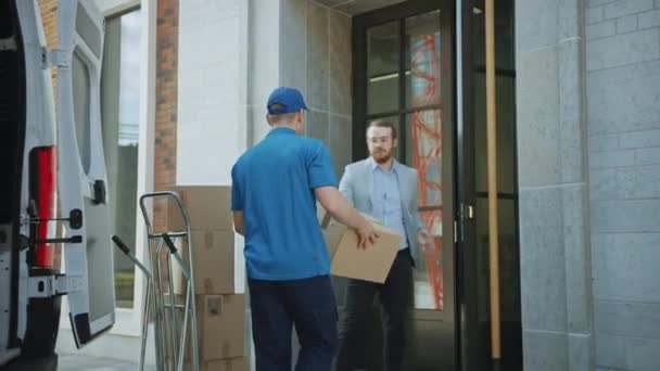 Bezorger geeft postpakket aan een zakelijke klant, die elektronische handtekening POD apparaat tekent. In stijlvolle moderne stedelijke kantooromgeving koerier bezorgt kartonnen doos Pakket aan een man — Stockvideo