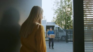 Delivery Man House ve Elektronik İmza Pod Cihazı İmzalayan Güzel Genç Kadına Karton Kutu Paketi Sunar. Arka planda Sevimli Banliyö Mahallesi. Yan Görünüm Yavaş Hareket Çekimi