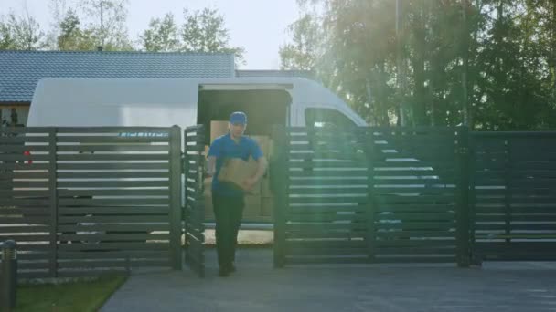 Der Zusteller mit dem Päckchen geht durch die Pforten, die das Postpaket ausliefern. im Hintergrund Lieferwagen in der Einfahrt der Vorstadtstraße — Stockvideo