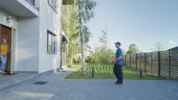 Delivery man House en levert kartonnen doos pakket aan een mooie jonge vrouw, die ondertekent elektronische handtekening pod apparaat. In de achtergrond schattig suburbane buurt. Zijaanzicht Slow Motion shot — Stockvideo