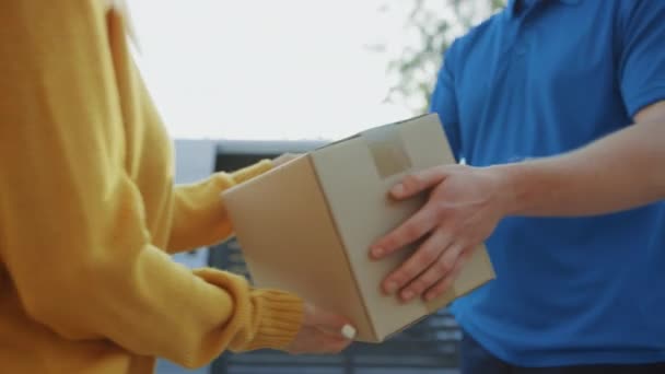 Piękna młoda kobieta spotyka Delivery Man, który daje jej karton Box Package, ona podpisuje elektroniczny podpis urządzenia pod. Przesyłka kurierska w dzielnicy podmiejskiej. Skoncentruj się na pudełku — Wideo stockowe