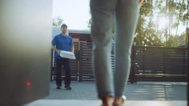 Bella giovane donna sorridente apre le porte della sua casa e incontra il ragazzo di consegna della pizza che le dà le sue scatole di cartone piene di gustosa pizza bollente. Angolo basso dopo colpo — Video Stock