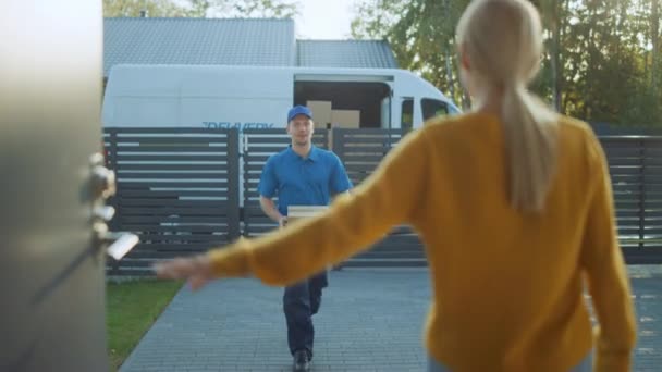 Mooie jonge vrouw opent deuren van haar huis en voldoet aan de levering Man die haar kartonnen doos postpakket geeft, ze tekent elektronische handtekening POD apparaat. — Stockvideo