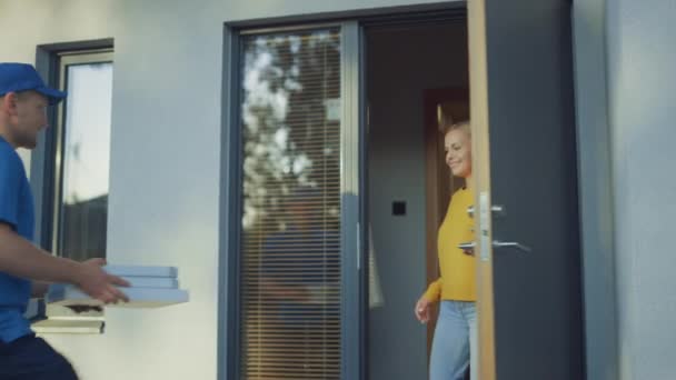 Krásná mladá usmívající se žena otevírá dveře svého domu a splňuje pizzu Muž, který dává její lepenkové krabice plné chutné páře pizza. — Stock video