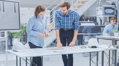 Endüstriyel Mühendislik Tesisi 'nde: Genç Kadın Tasarımcı, Endüstriyel Mühendisle Çalışıyor, Masa üzerinde yatan Tartışma, Analiz ve Doğru Motor Tasarım Teknik Tasarımları var