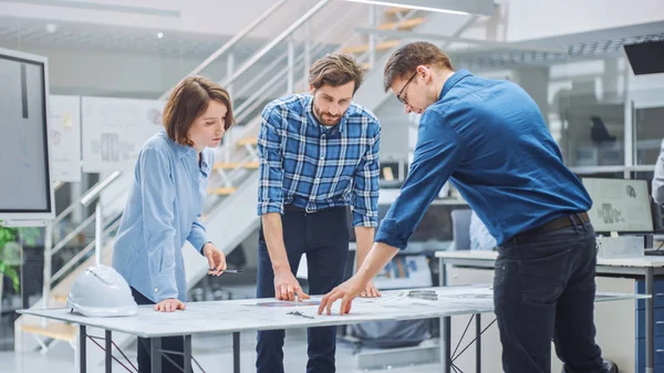 In the Industrial Engineering Facility: Female Designer Works with Industrial Engineer and Master Technician, They have Discussion, Analyse Engine Design Technical Drafts that Lying on the Table — 스톡 사진