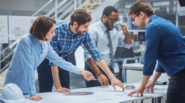 In the Industrial Engineering Facility: Diverse Group of Engineers, Technicians, and Specialists on a Meeting, Have Discussion, Analyse Engine Design Technical Drafts that are lying on the table — 图库照片