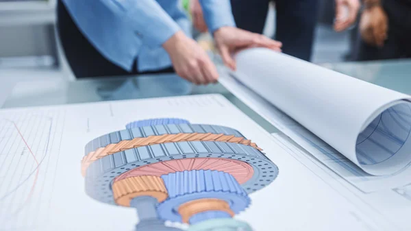 In the Industrial Engineering Facility: Diverse Group of Engineers and Technicians on a Meeting Gather Around Table Unravel Sheets of Engine Design Technical Drafts, Have Discussion, Analyse Drawings