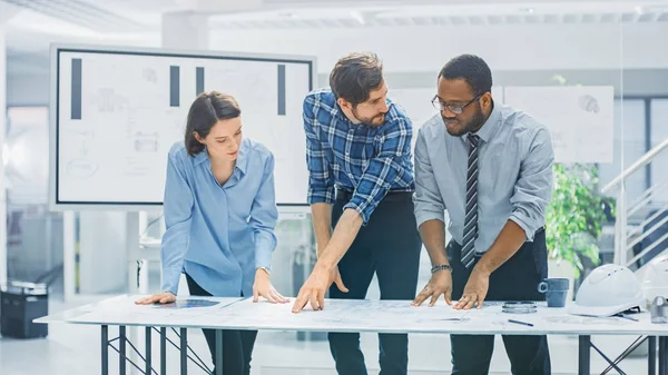 En la Instalación de Ingeniería Industrial: Diverso Grupo de Ingenieros y Técnicos en una Reunión Reúnase Alrededor de la Mesa Desentrañar Hojas de Diseño de Motores Redacciones Técnicas, Tener Discusión, Analizar Dibujos — Foto de Stock