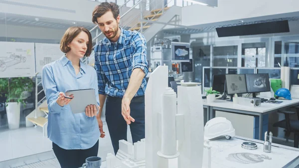 En Architectural Bureau: Arquitecto e Ingeniero Hablando, Usando Tablet Computadora Digital, Trabajando en un Proyecto de Prototipo Complejo de Edificios, Usando Modelo de Ciudad y Computadoras Ejecutando Software CAD 3D — Foto de Stock