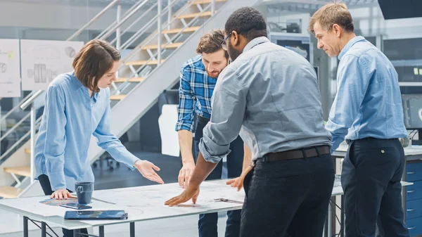 In the Industrial Engineering Facility: Diverse Group of Engineers and Technicians on a Meeting Around Table Unravel Sheets of Engine Design Technical Drafts, Have Discussion, Analyse Drawings. — 스톡 사진