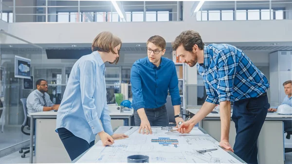 Dans l'installation de génie industriel : Designer féminin travaille avec l'ingénieur industriel et le maître technicien, Ils ont une discussion, Analysent les projets techniques de conception de moteur qui reposent sur la table — Photo