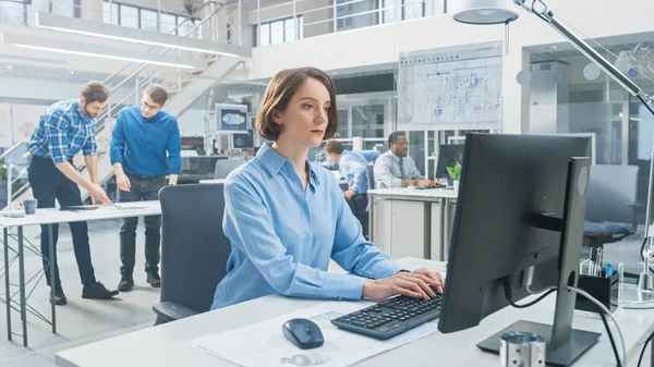 Na Instalação de Engenharia Industrial: Retrato da Engenheira Inteligente e Bela que Trabalha no Computador Desktop. No fundo Especialistas e técnicos que trabalham com rascunhos e desenhos — Fotografia de Stock