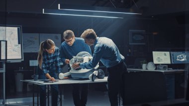 Gece geç saatlerde Robot Mühendisliği Tesisi Üç Teknik Mühendisler Tekerlekli Robot Prototipi hakkında konuşuyor ve çalışıyor. Arkaplan Yüksek Teknoloji Araştırma Merkezi Ekranları Endüstriyel Tasarımı Gösteriyor
