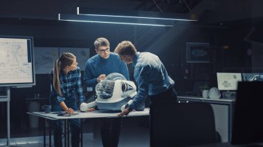 Gece geç saatlerde Robot Mühendisliği Tesisi Üç Teknik Mühendisler Tekerlekli Robot Prototipi hakkında konuşuyor ve çalışıyor. Arkaplan Yüksek Teknoloji Araştırma Merkezi Ekranları Endüstriyel Tasarımı Gösteriyor