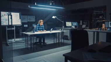 Masasında Masasında Oturan Kadın Mühendis Bir Masanın Üzerinde Planlarla Çalışıyor, Kalem, Cetvel ve Dijital Tablet Kullanıyor ve Kahve İçiyor. Karanlık Endüstriyel Tasarım Mühendislik Tesisinde