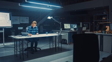 Masasında Oturan Kadın Mühendis Tablet, Cetvel, Cetvel ve Dijital Tablet Kullanarak Tablo Üzerinde Uzanan Planlarla Çalışıyor. Karanlık Endüstriyel Tasarım Mühendislik Tesisinde