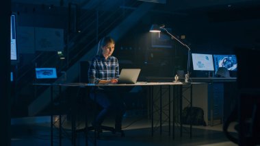 Masasında oturan güzel bayan mühendis bir dizüstü bilgisayarla çalışıyor. Bir Masanın Üzerinde Yatan Planlar. Karanlık Endüstriyel Tasarım Mühendislik Tesisi 'nde. Sıcak Işık Lambası