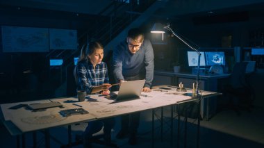 Endüstriyel Mühendislik Tesisi: Masaüstü Bilgisayarında Çalışan Kadın Mühendis, Proje Yöneticisi Görev ve Proje Detayları 'nın Yanında Duruyor ve Açıklıyor. Motor Prototipi Üzerinde Geç Çalışma