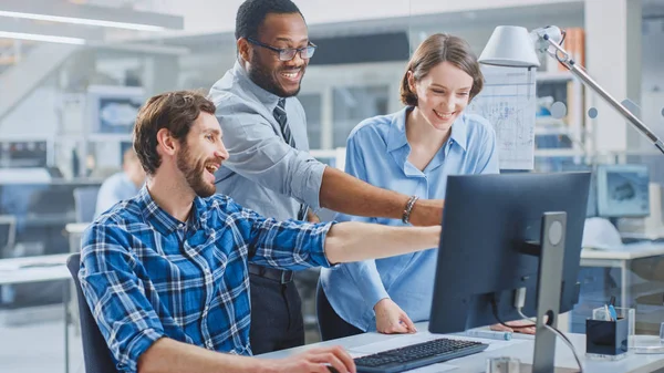 In the Industrial Engineering Facility: Male Engineer Working on Desktop Computer, Female Chief Engineer and Project Manager Discuss and Explain to Him Project Details. They Smile, Joke and Cheer — Stock Photo, Image