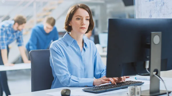 In the Industrial Engineering Facility: Portrait of the Smart and Beautiful Female Engineer Working on Desktop Computer. In the Background Specialists and Technicians Working with Drafts and Drawings — Stock Photo, Image