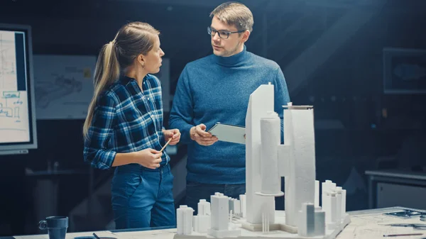 В творческом архитектурном бюро работают два профессиональных инженера по модели городского округа. Городские планировщики работают над функциональной моделью здания. Они говорят и используют цифровой планшетный компьютер — стоковое фото