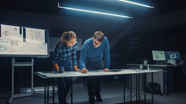 V Dark Industrial Design Engineering Facility mužští a ženští inženýři mluví a pracují na plánech pomocí digitálního tabletu a konferenčního stolu. Na ploše kresby a součásti motoru — Stock fotografie