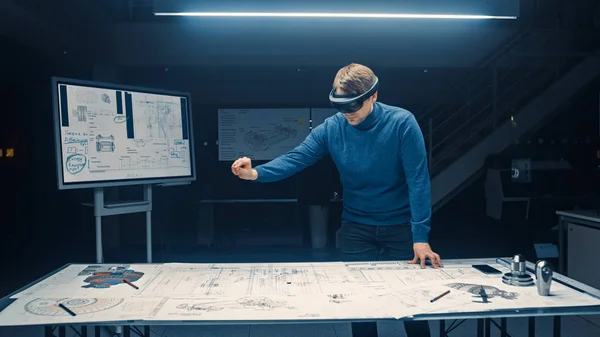 Software Development Engineer Wearing Virtual Reality Headset Gestures and Manipulates Components in Augmented Reality. Engineering Facility Has Desk with Engine and Car Concept Blueprints — Stock Photo, Image