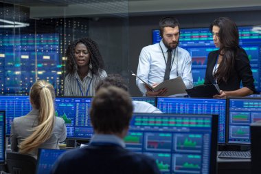 Tüccarlar çok etnik gruptan oluşan takım meşgul Menkul Kıymetler Borsası ofisinde çalışıyor. Bayi ve Broker satın almak ve satmak hisse senetleri piyasasında. Monitörler ilgili Infographics, veri ve sayıların görüntüsünü.