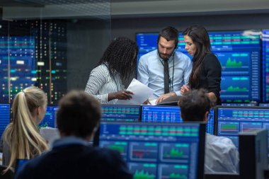 Tüccarlar çok etnik gruptan oluşan takım meşgul Menkul Kıymetler Borsası ofisinde çalışıyor. Bayi ve Broker satın almak ve satmak hisse senetleri piyasasında. Monitörler ilgili Infographics, veri ve sayıların görüntüsünü.