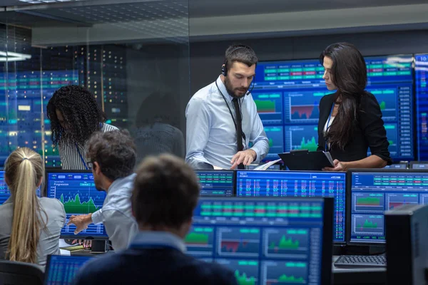 Multi-Ethnic Team of Traders is Busy Working at the Stock Exchange Office. Dealers and Brokers Buy and Sell Stocks on the Market. Monitors Display Relevant Infographics, Data and Numbers.