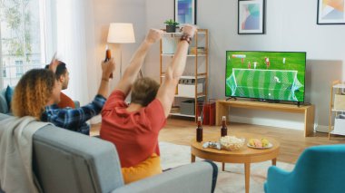 Oturma odasında bir koltukta oturan üç spor fanatiği televizyonda önemli futbol maçlarını izleyip, takımları için tezahürat yapan, takımına galibiyet getirdikten sonra 