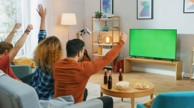 Oturma Odasında Üç Arkadaş Yeşil Kroma Anahtar Ekranı 'nda Video Oyunları Oynuyor, Kontrolörler ve Kutlayanlar Kazanarak Evet Hareketi Yapıyor ve Kolları Kaldırıyor. Gençler Evlerinde Eğleniyor.