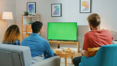Çeşitli Arkadaş Grubu Evdeki Koltukta Oturuyor, Atıştırmalık ve içecek yerken Yeşil Krom Anahtar Ekran TV izliyor. Gençler Evlerinde Eğleniyor.