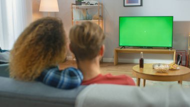 Evde oturup Yeşil Krom Anahtar Ekranı 'nı izleyen ve koltukta dinlenen mutlu çift. Çift Oda İzleme Spor Maçı, Haberler, Sitcom TV Şovu veya Bir Film.