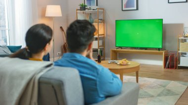 Evde oturup Yeşil Kroma Anahtar Ekran Televizyonu 'nu izleyen ve koltukta dinlenen mutlu çift. Çift Oda İzleme Spor Oyunu, Haberler, Sitcom TV Şovu veya Bir Film.