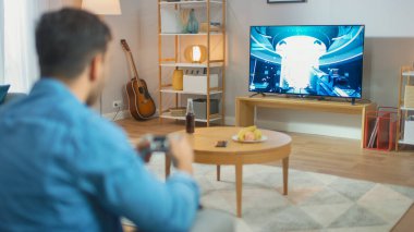Oturma Odasında Oturan Koltuk Tutucu Denetleyicisinde Bir Konsol Video Oyunu 'nda Oynayan 3d Eylem Atıcısı Oyunu TV' de gösterildi.